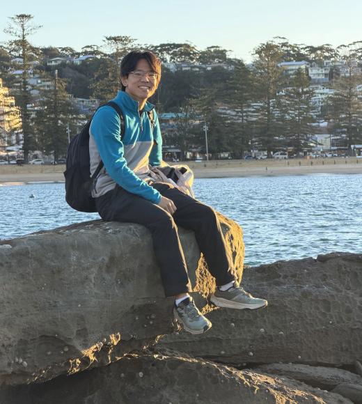 Young person sitting on large rock by snowy shoreline at golden hour with backpack